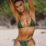 Woman in a green bikini sitting under a palm tree on a beach
