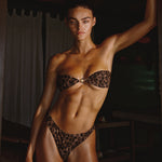 Model wearing a leopard print bikini in a dimly lit room.